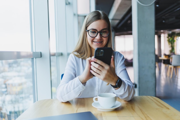 Heureuse femme gérante souriante utilisant un gadget de téléphone portable pour vérifier le service de livraison via une application en ligne réseau sans fil 4g gratuit dans un café joyeuse pigiste envoyant des SMS sur un téléphone portable