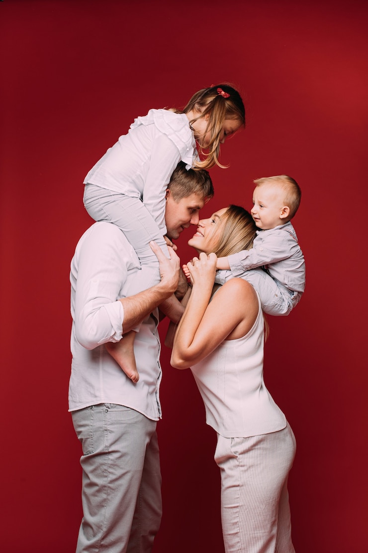 Photo heureuse femme et homme debout sur le rouge avec leur nez touchant. les enfants assis sur leurs épaules.