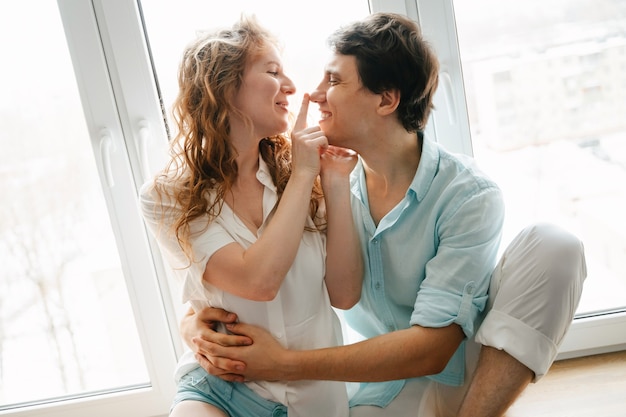 Heureuse femme et homme s'embrassant près de la fenêtre à la maison le jour de la Saint-Valentin