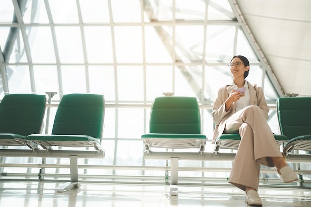 Heureuse femme intelligente souriante et utilisant un smartphone dans le concept de voyage d'affaires passagère fille voyageant au travail femme d'affaires en attente d'un vol dans le terminal de l'aérodrome de l'aéroport