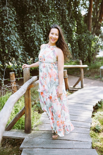 Heureuse femme japonaise métisse en robe maxi florale romantique dans le parc