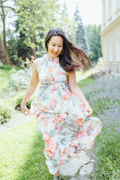 Heureuse femme japonaise multiraciale en robe maxi florale romantique dans le parc d'été