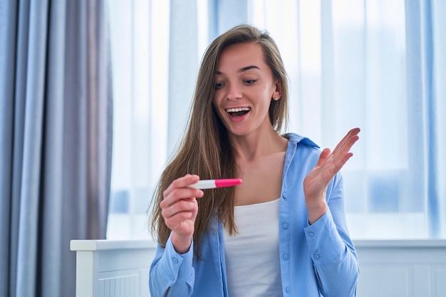 Heureuse femme joyeuse satisfaite se réjouit d'un test de grossesse positif. Grossesse souhaitée planifiée et attendue depuis longtemps