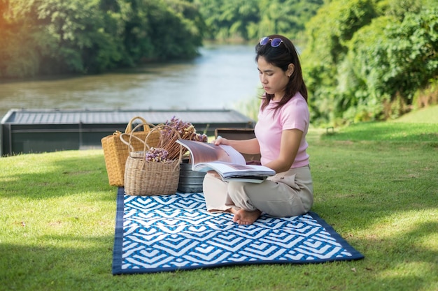 Heureuse femme lisant un livre à l'heure du pique-nique dans le parc près de la rivière Concept de printemps et de vacances d'été