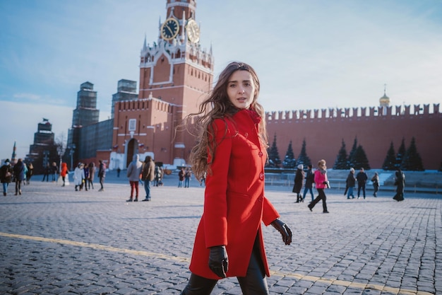 Heureuse femme marchant en manteau rouge sur la place rouge à Moscou Temps froid entre l'hiver et le printemps, le gel et le soleil