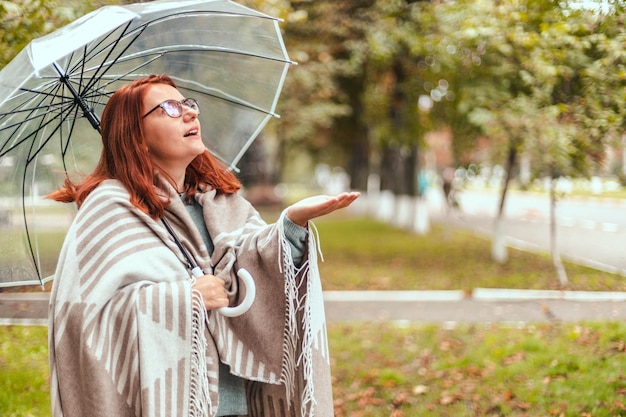 Heureuse femme marchant avec un parapluie transparent sous la pluie au parc de la ville d'automne par temps pluvieux