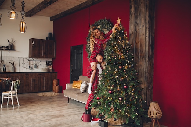 Heureuse femme et mari dans des vêtements assortis aidant la maison ornée ensemble la veille de Noël