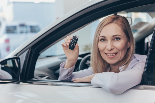 Heureuse femme mature assise dans sa nouvelle voiture détenant la clé de voiture