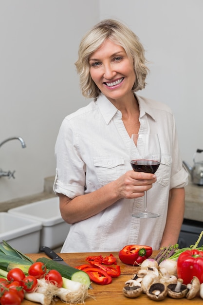 Heureuse femme mature avec des légumes et du verre de vin dans la cuisine