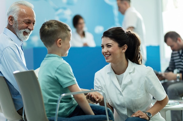 Heureuse femme médecin parlant à un petit garçon qui est venu avec son grand-père pour un rendez-vous médical à la clinique