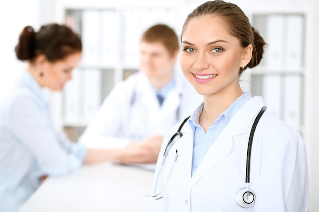 Heureuse femme médecin avec le personnel médical de l'hôpital assis à la table et discutant des antécédents médicaux