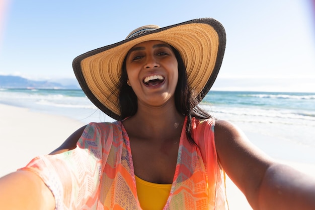 Heureuse femme métisse en vacances à la plage prenant le selfie. vacances de loisirs en plein air au bord de la mer.