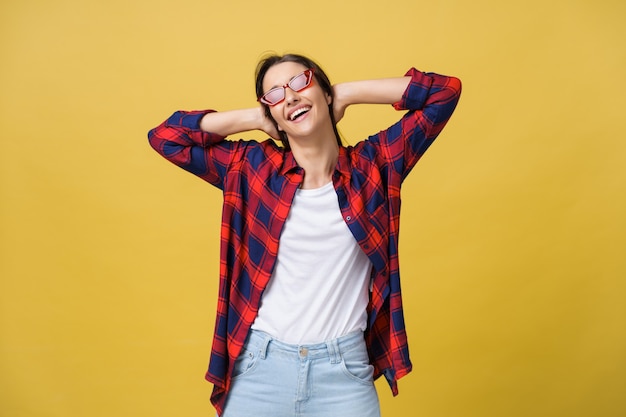 Heureuse femme moderne et élégante avec des lunettes de soleil de forme moderne riant en vous regardant la caméra isolée sur fond jaune. Notion de bonheur