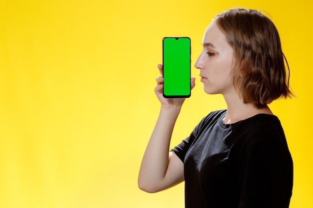 Heureuse femme montrant un smartphone avec écran vert, application de réseau social.