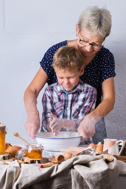 Photo heureuse femme mûre âgée, grand-mère et jeune garçon, petit-fils cuisinant, pétrissant la pâte, tarte au four, gâteau, biscuits. moment en famille dans la cuisine confortable. activité d'automne à la maison.