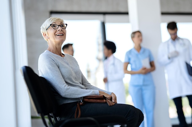 Heureuse femme mûre assise dans une salle d'attente à la clinique médicale