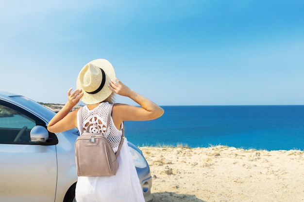 Heureuse femme mûre au chapeau debout près de la voiture et profiter des vacances d'été