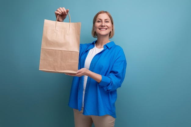 Heureuse femme mûre tenant un sac artisanal pour faire du shopping sur l'espace de copie de fond bleu