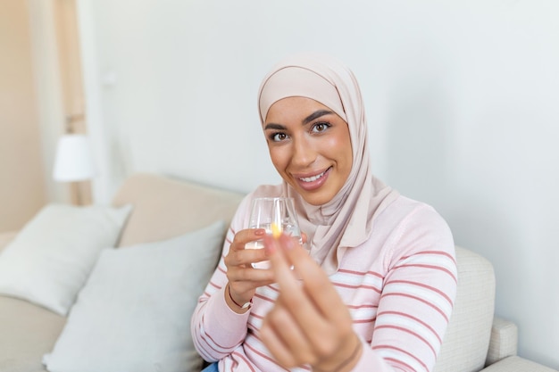 Heureuse femme musulmane arabe montrant une pilule de supplément de vitamines et un verre d'eau regardant la caméra