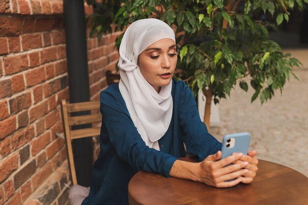 Heureuse femme musulmane ayant un appel vidéo sur smartphone en ville