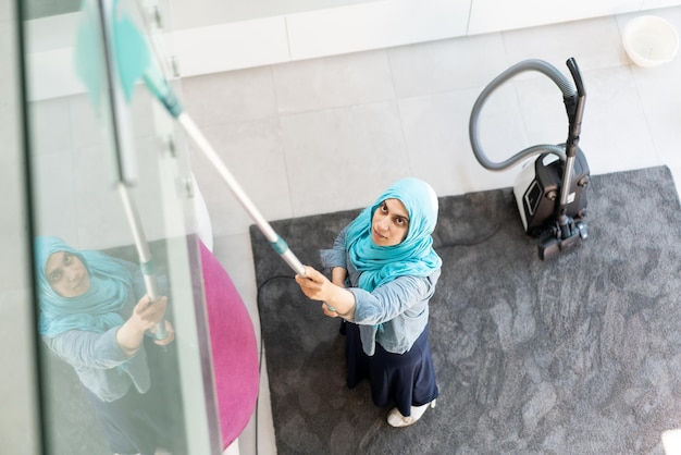 Heureuse femme musulmane nettoyant le salon de la maison moderne. Photo de haute qualité