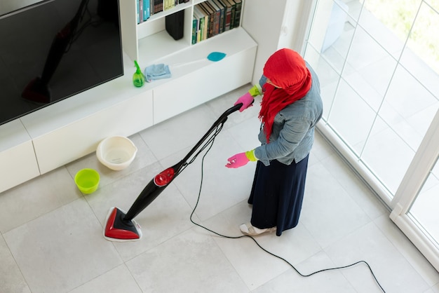 Heureuse femme musulmane nettoyant le salon de la maison moderne. Photo de haute qualité