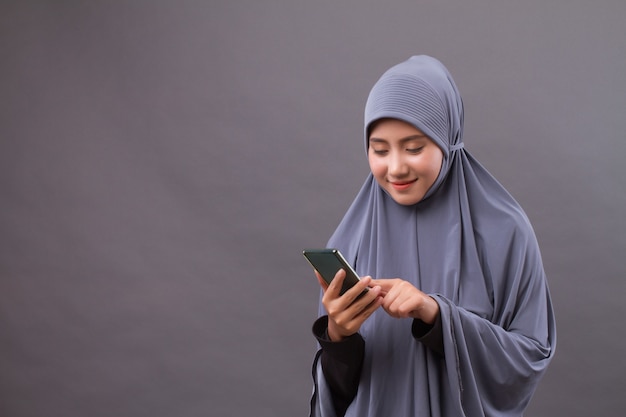 Heureuse femme musulmane souriante à l'aide de smartphone, appareil Internet sans fil