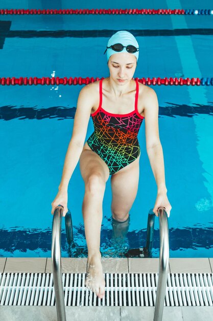 Heureuse femme nageuse musclée en lunettes et bonnet dans la piscine et représente le concept de santé et de bonne forme Beau modèle féminin dans l'eau faisant de la natation synchronisée