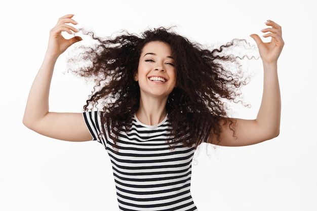 Heureuse femme naturelle jouant avec les cheveux, souriant dansant et riant, s'amusant sur fond blanc