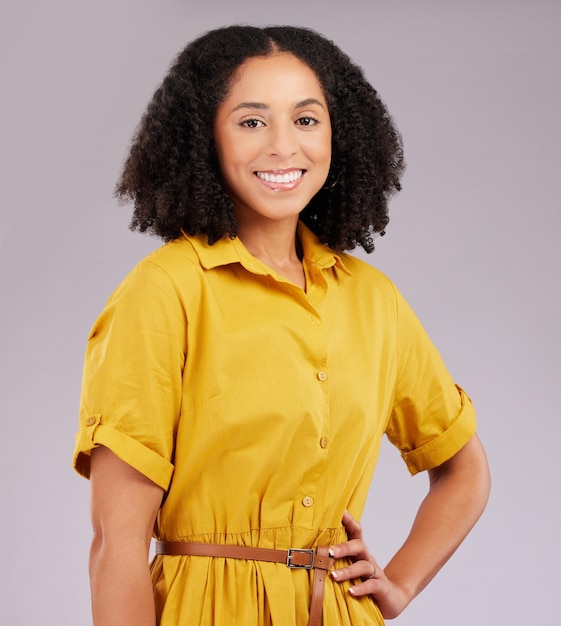 Heureuse femme noire confiante et portrait sourire debout avec les mains sur la taille sur un fond de studio gris Modèle féminin afro-américain isolé et élégant avec afro souriant en toute confiance