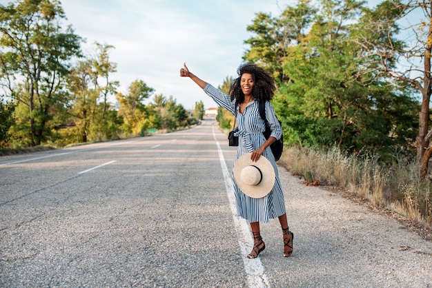 Heureuse femme noire faisant de l'auto-stop avec les pouces vers le haut