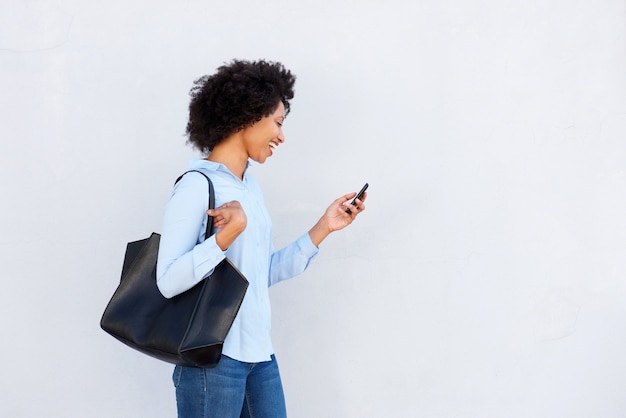 Heureuse femme noire marchant avec téléphone portable et sac à main sur fond gris