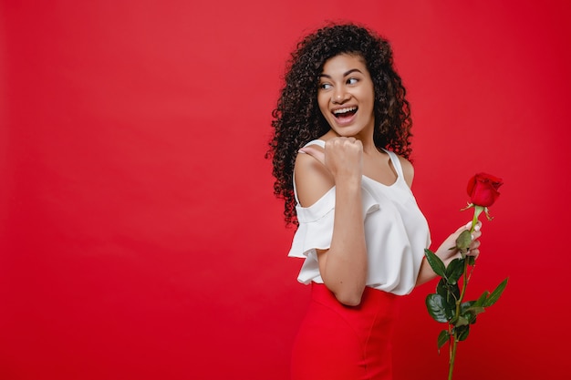 Heureuse femme noire souriante avec rose rouge à la main isolé sur rouge