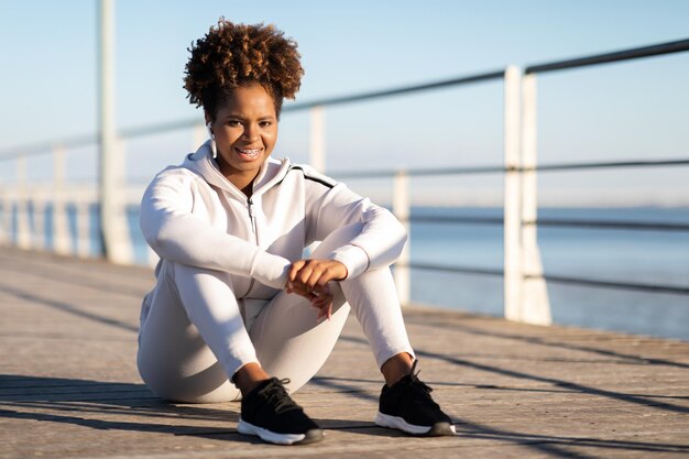 Photo heureuse femme noire sportive en vêtements de sport se détendre après un entraînement de fitness à l'extérieur