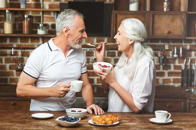 Heureuse femme nourrissant l'homme avec de la farine d'avoine à la cuisine