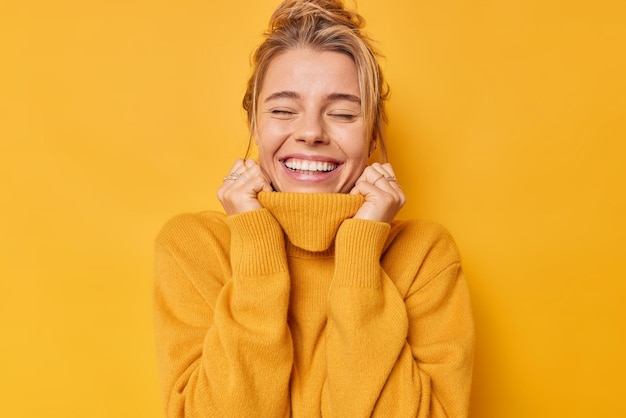 Photo heureuse femme optimiste garde les yeux fermés sourit doucement rêverie tient les mains sur le col du cavalier rappelle de beaux souvenirs isolés sur fond jaune vif respire librement. émotions insouciantes.