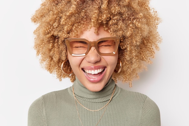 Heureuse femme optimiste rit joyeusement louches le visage se sent joyeux entend quelque chose de drôle sourit largement porte des lunettes et poloneck isolé sur fond blanc. Concept d'émotions sincères.