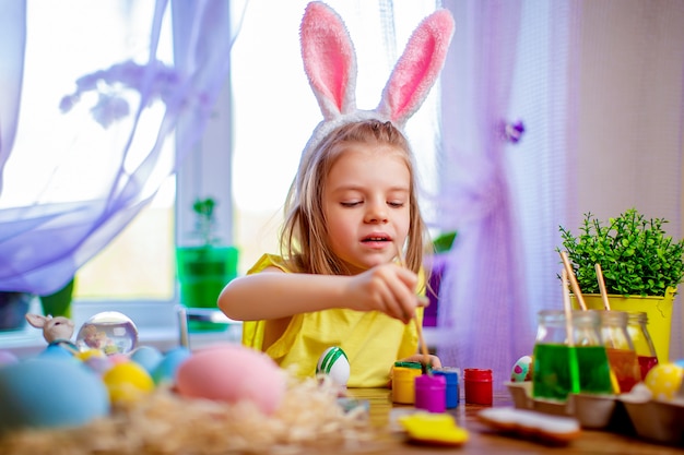 Heureuse femme de Pâques dans les oreilles de lapin peignant des oeufs, petit enfant à la maison. Vacances de printemps