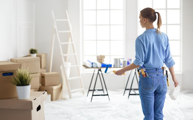 Heureuse femme peint mur avec rouleau à la maison