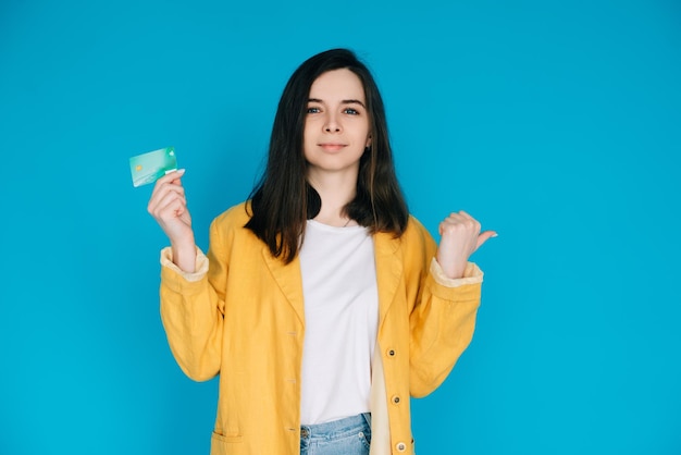 Heureuse femme pointant le pouce vers l'espace vide avec carte de crédit femme positive et attrayante exprimant