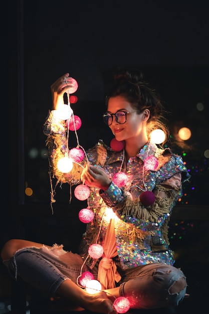 Heureuse femme portant une veste rougeoyante avec des paillettes tient des boules de lumière dans ses mains