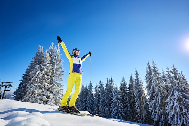 Heureuse femme posant sur des skis avant de skier. Journée ensoleillée à la station de ski. Ciel bleu clair, sapins couverts de neige sur fond.