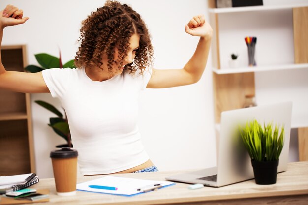 Photo heureuse femme positive avec des boucles sur la tête travaillant au bureau sur un ordinateur portable