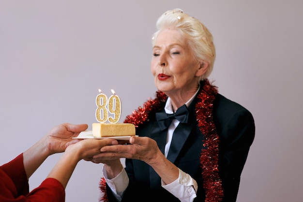 Heureuse femme de quatre-vingt-neuf ans élégante et joyeuse en costume noir célébrant son anniversaire avec un gâteau