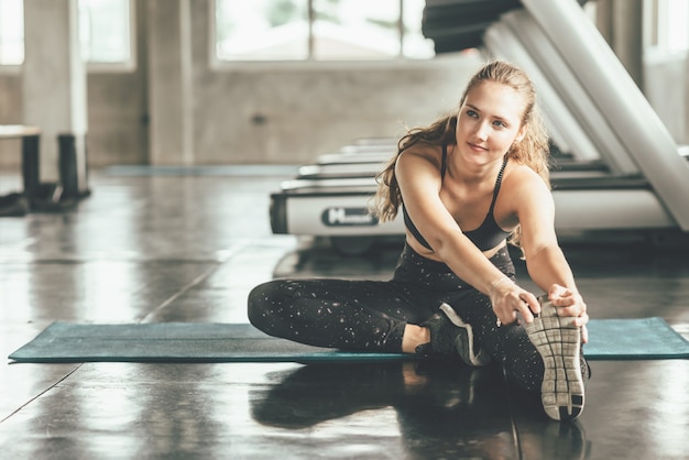 Heureuse femme qui s&#39;étend de la jambe au gymnase