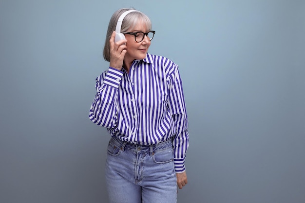 Heureuse femme retraitée aux cheveux gris avec un casque sur un fond de studio lumineux