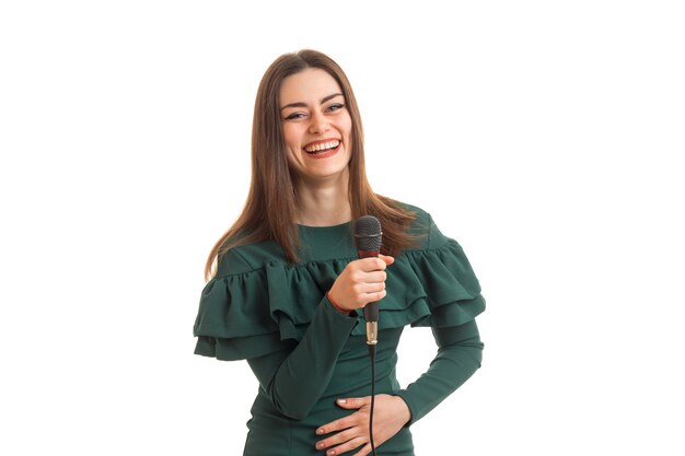 Heureuse femme riant avec microphone dans les mains en robe verte isolée sur fond blanc