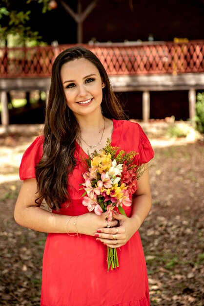 Heureuse femme en robe rouge tenant un bouquet de fleurs