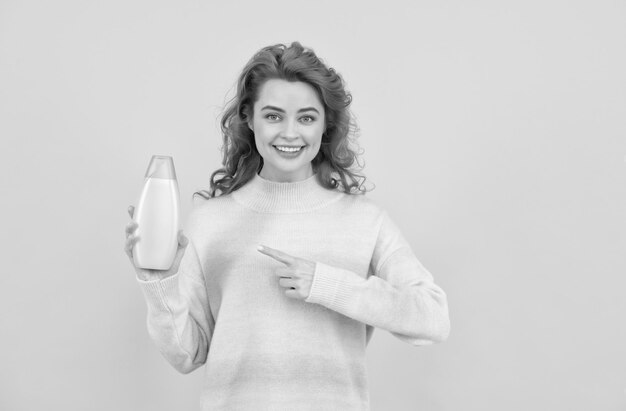 Heureuse femme rousse aux cheveux bouclés pointant le doigt sur la beauté du shampooing ou de l'après-shampooing