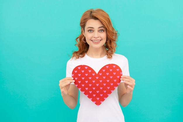 Heureuse femme rousse tenir coeur rouge sur fond bleu